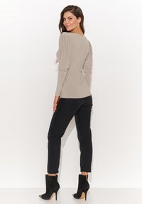 Beżowa bluzka z długim rękawem, kwadratowym dekoltem i marszczonymi ramionami, połączona z czarnymi dżinsami i czarnymi botkami za kostkę. Gładka tekstura.