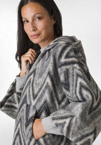 Grå og creme mønstret poncho med hætte, lavet af blød uld, med løs pasform og strikdetaljer på manchetterne.