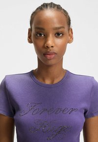 Paarse geribbelde t-shirt met korte mouwen en ronde hals, met 'Forever Hugo' in zwarte rhinestones op de voorkant.