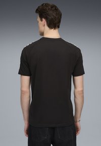 Sort kortærmet t-shirt med teksturerede pynteløsninger langs skuldrene, klassisk rund halsudskæring og en glat bomuldsstof.