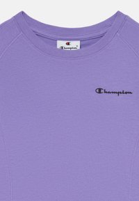 T-shirt champion violet avec un col rond côtelé et un logo noir. Tissu doux et léger avec une texture subtile et une coupe ajustée.
