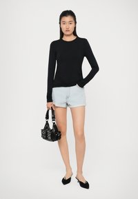 Maglietta nera a maniche lunghe, pantaloni corti in denim azzurri, mule nere con tacco, e una piccola borsa nera con borchie argento. Design semplice e aderente.