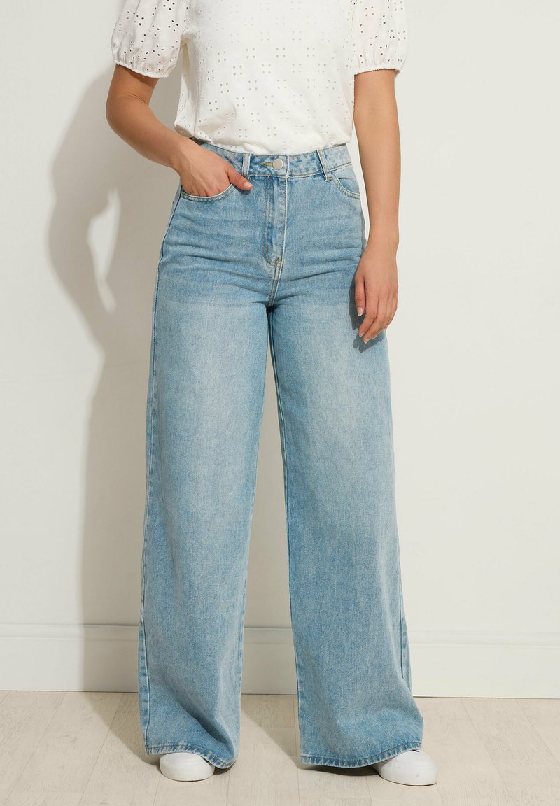 Jeans de tiro alto y pierna ancha en azul claro con una textura de denim suave, que cuentan con bolsillos frontales y un cierre de un solo botón de metal.