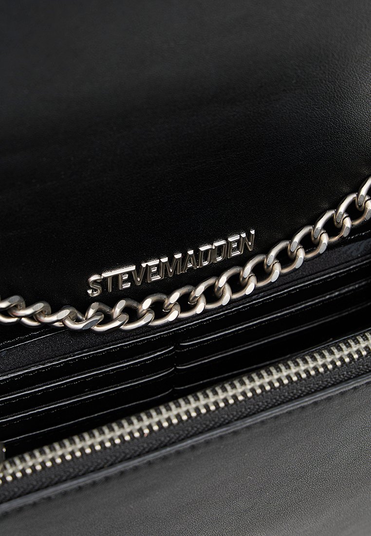 Portafoglio in pelle nera con zip argentata, dettaglio a catena e nome del marchio "Steve Madden" inciso all'interno.