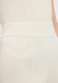 Pantalons en tissu crème avec une taille large, une texture lisse et des coutures verticales pour une silhouette ajustée.