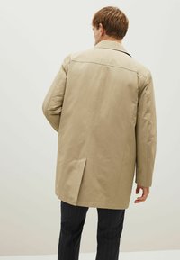 Lys beige trench coat med lige snit, lange ærmer og klapkrave. Har en slids bagtil og en glat tekstur.