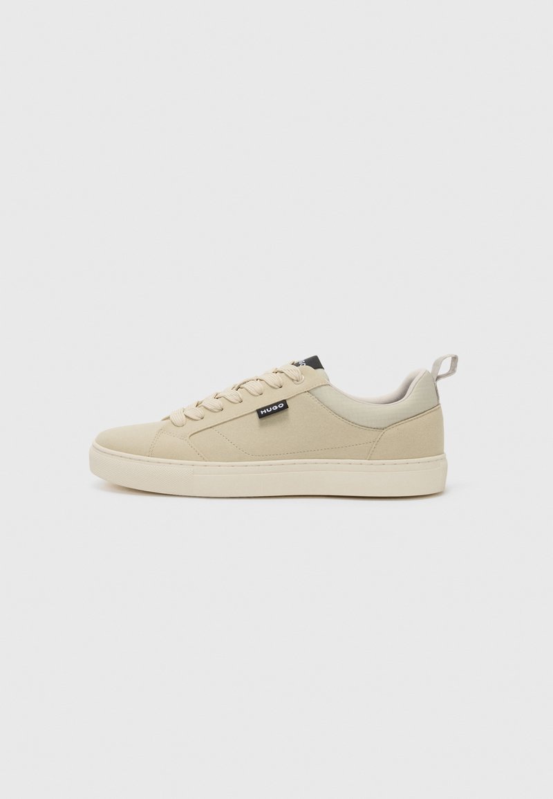 Beige sneakers with a smooth fabric upper, round toe, lace-up front, and a logo tag on the side. The sole is thick and designed for comfort.