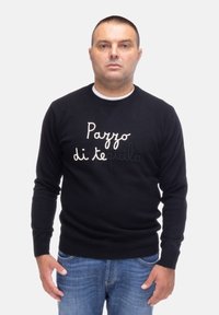 Maglione nero con collo tondo, con testo ricamato bianco "Pazzo di tequila" sulla parte frontale, abbinato a jeans blu.