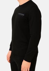 Felpa nera in tessuto morbido, con scollo rotondo, polsini a coste e un discreto logo Cristiano Ronaldo Nightwear sul davanti.