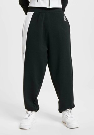 Black sweatpants with a tapered fit, featuring a white side panel, elastic waistband, and smooth cotton blend fabric. Pairing with white sneakers.