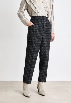 Personne portant un pantalon à carreaux noir et blanc taille haute avec des poches, un chemisier beige texturé et des bottines à talons en daim beige.