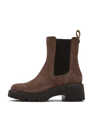 Bota de tobillo de ante marrón con paneles laterales elásticos, una tirador y una suela de goma negra gruesa con un patrón de relieve texturizado.
