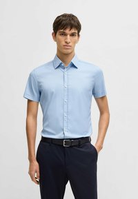 Lichtblauw overhemd met korte mouwen, met een klassieke kraag, gemaakt van een soepele stof, gepresenteerd met een zwarte riem en donkere broek.