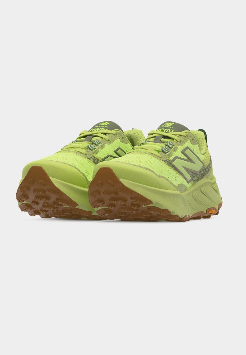 Par de zapatillas de trail running de neón verde con suelas marrones texturizadas y logotipos "N" grises, mostradas desde un ángulo frontal.