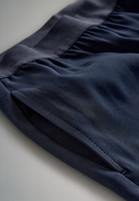 Shorts en tissu bleu marine avec une ceinture lisse, une texture plissée et des coutures nettes. Dotés d'entailles latérales pour faciliter les mouvements.
