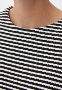 Svart, vit och gulrandig stickad duk med en grov textur och en rundad halsringning, med fokus på horisontella linjer.