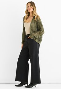 Olive green open-knit cardigan over a beige fitted top, paired with high-waisted black wide-leg jeans and black pointed-toe heels.