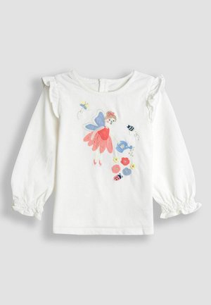 Hvid langærmet tumbler-skjorte med flæser på skuldrene, prydet med en farverig fe med vinger, der vander broderede blomster og insekter.