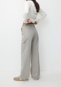 Pantaloni cargo grigi chiari a gamba larga con tasche laterali e vita alta. Tessuto morbido con una texture liscia. Abbinati a un maglione bianco e sneakers.