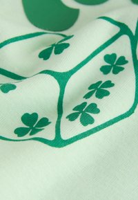 Tela de algodón verde con un patrón de tréboles de cuatro hojas y formas redondeadas sobre un fondo verde claro con una textura suave.