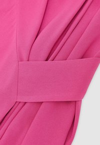 Tela de color rosa brillante con un detalle de cinturón ancho que ajusta pliegues recogidos, mostrando la textura y las costuras en un material liso y fluido.