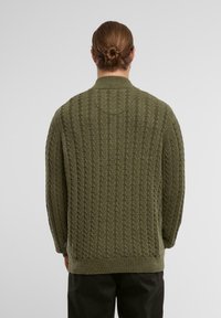 Olijfgroen gebreide trui met een textuur kabelontwerp. Heeft een ronde hals en ribgebreide manchetten en zoom. Gevisualiseerd vanuit de achterkant.