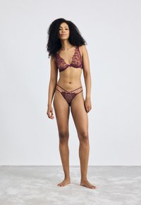 Ensemble de lingerie en dentelle de couleur bordeaux profond avec des motifs floraux, présentant un décolleté plongeant et des bretelles ajustables. Tissu lisse et semi-transparent.