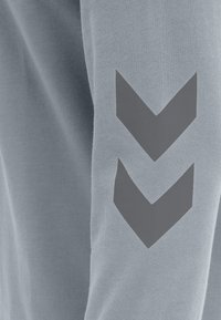 Camicia a maniche lunghe azzurro chiaro in cotone, con un design a zig zag grigio sulla manica sinistra, dalla texture morbida e dal taglio casual.