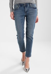 Jeans in denim blu chiaro con vestibilità slim, dotati di tasche frontali e dettagli sbiaditi. Abbinati a scarpe con tacchi alti argento.