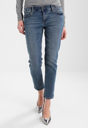 Jean en denim bleu clair avec une coupe slim, dotés de poches avant et de détails délavés. Assortis à des chaussures à talons hauts argentées.