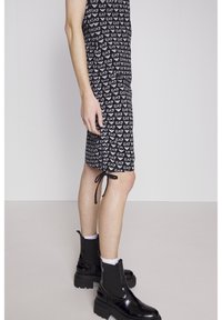 Svart klänning med upprepat vitt EA7-logomönster. Har sidoknytning vid fållen och kombineras med svarta kraftiga ankle boots och vita strumpor.