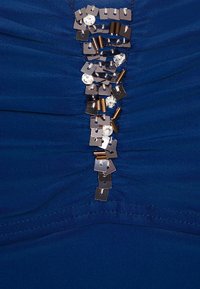 Tissu bleu présentant des fronces avec un ornement central composé de sequins et de pièces métalliques créant un effet de design en couches.