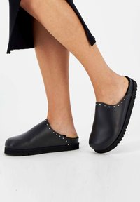 Black leather clogs with a smooth finish, low heel, and decorative silver studs along the top edge; slip-on design for easy wear.