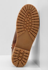 Botte marron avec une semelle en caoutchouc texturée ornée de motifs en forme d'étoile, le nom de la marque "ANNA FIELD" et la taille "37" embossés en dessous.