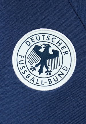 Besticktes Deutscher Fußball-Bund Adler-Logo auf dunkelblauem Stoff, rund mit fetten schwarzen Buchstaben und weißem Hintergrund.