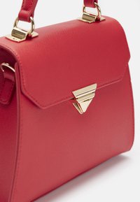Czerwona torebka skórzana o teksturze z złotym trójkątnym zapięciem i pasującymi złotymi elementami mocującymi uchwyt.