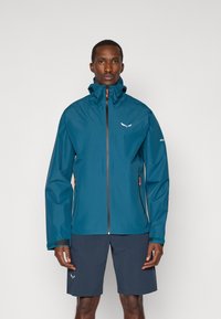 Τηλαίνα αδιάβροχη ζακέτα με μπροστινό φερμουάρ, ρυθμιζόμενη κουκούλα και πορτοκαλί pull zippers. Διαθέτει πλαϊνές τσέπες και μια διακριτική λογότυπο στο στήθος.