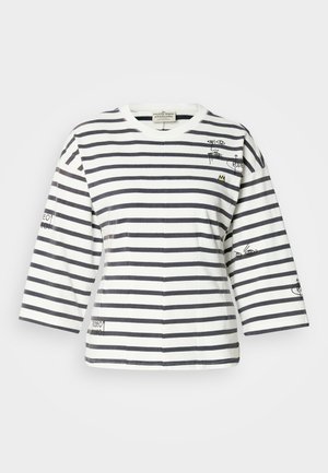 Csíkos pamut póló tengerészkék és fehér csíkokkal, háromnegyedes ujjakkal, kerek nyakkivágással, valamint szemekkel és felirattal díszített grafikával az ujjakon.