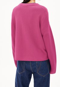 Pull en maille rose à coupe décontractée, col rond et texture côtelée, assorti à un jean bleu foncé taille haute avec poches arrière.