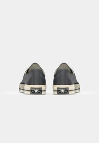 Sivi platneni slip-on tenisice s okruglim prstima, gumene potplate i izblijedjelim bijelim akcentima. Imaju crnu oznaku loga na peti.