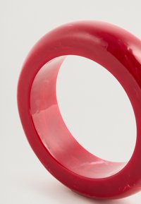 Červený kruhový prsten vyrobený z lesklého materiálu, s pevným tvarom a hladkým povrchom, s jemnými farebnými variáciami.