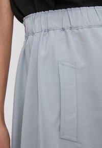 Jupe bleu clair avec une taille élastique, dotée d'une poche plate sur le côté. Le tissu a une texture lisse et un éclat subtil.