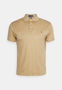 Beige polo skjorta i mjuk bomull, med en tre-knapplåsning, korta ärmar och en liten broderad logotyp på vänster bröst.