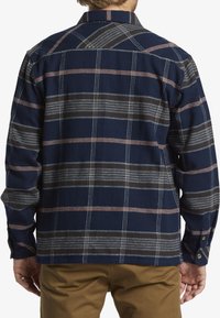 Camisa de franela azul oscuro con un patrón de cuadros que presenta rayas en gris, blanco y color óxido. Cuello clásico y puños con botones.