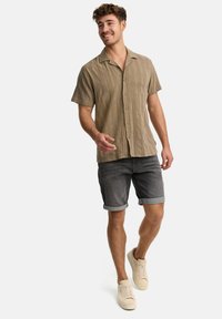 Korte mouwen lichtbruine geweven shirt met een kraag, knoopsluiting aan de voorkant, gecombineerd met opgerolde denimshorts en beige sneakers.