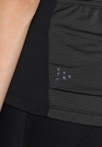 Černé sportovní oblečení s texturovaným designem a horizontálními pruhy. Výrazným detailem je logo s prošívanými tečkami na boku.