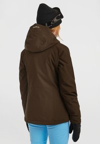 Bruine waterdichte jas met een capuchon en verstelbare elementen, gecombineerd met blauwe broek en zwarte handschoenen, ontworpen voor winteractiviteiten.