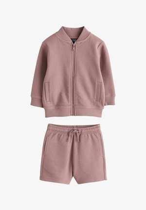 Roza teksturirana pletena jakna na patentni zatvarač s dugim rukavima i odgovarajuće kratke hlače sa špagama, oba komada imaju bočne džepove.