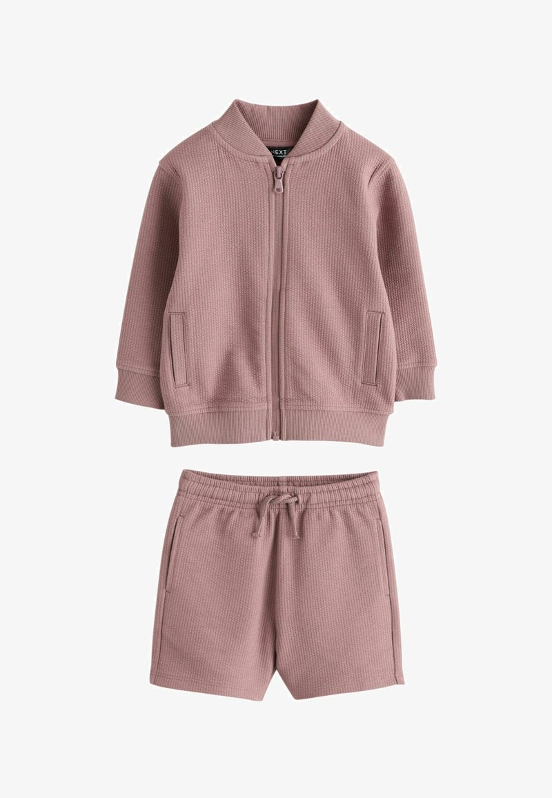 Veste zippée en maille texturée rose à manches longues, associée à un short à cordon assorti, tous deux dotés de poches latérales.