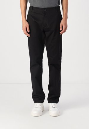 Pantalones de algodón negros con un diseño de pierna recta, que cuentan con un cierre de botón y bolsillos laterales. Llevados con zapatillas blancas.
